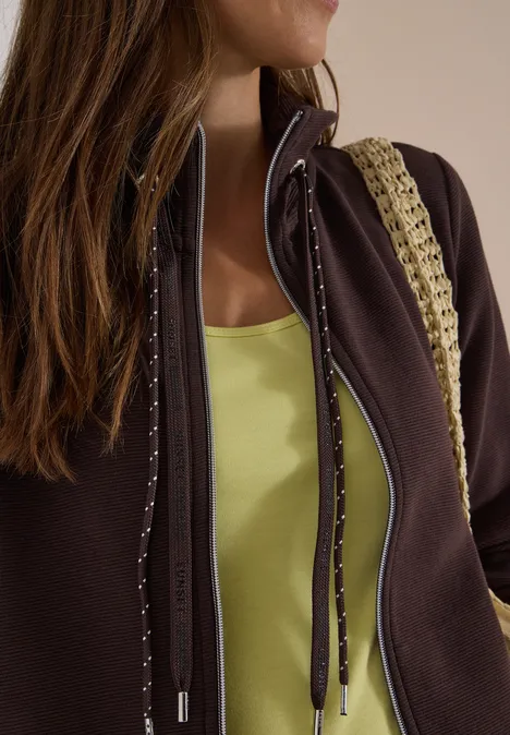 Femme en veste marron, top vert clair et bandoulière au crochet.