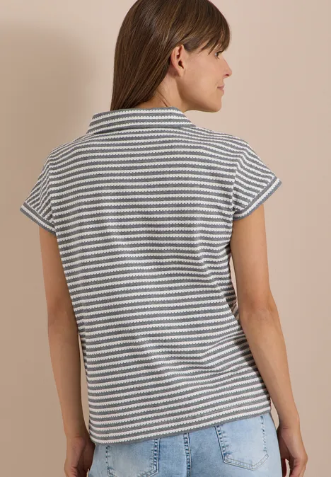 Frau steht seitlich, Rücken zur Kamera, trägt gestreiftes Kurzarmshirt und helle Jeans.