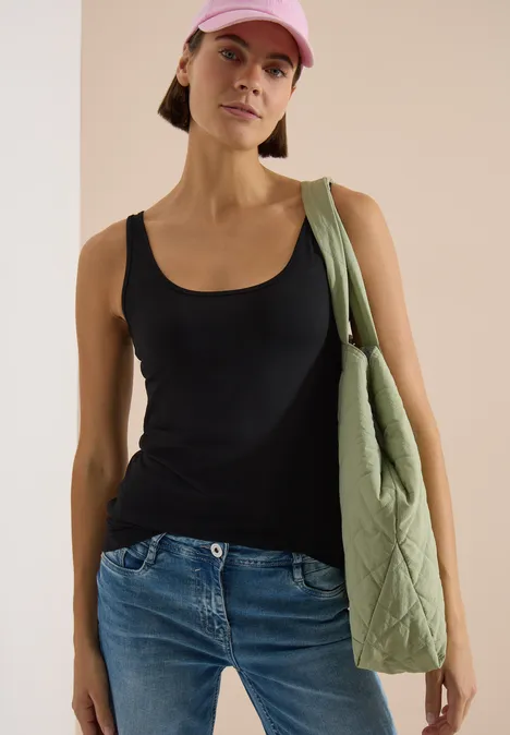 Femme en top noir et jean, avec un sac vert matelassé porté à l'épaule et une casquette rose.