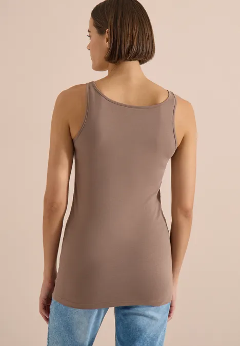 Vue de dos d'une femme portant un débardeur taupe et un jean devant un fond beige.