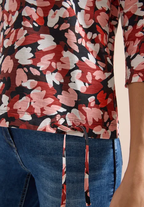 Rotes und weißes Blumenmuster auf schwarzem 3/4-Arm-Shirt kombiniert mit blauen Jeans.