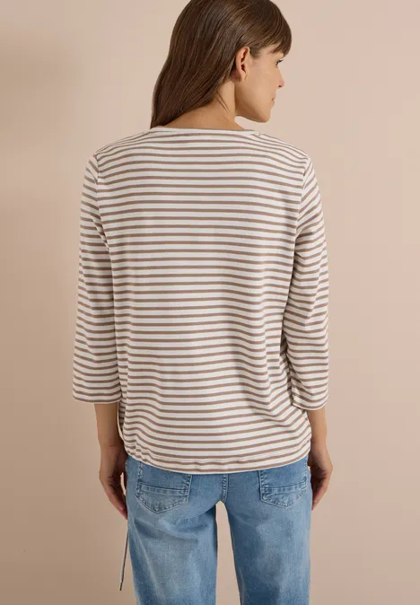 Frau steht mit dem Rücken zur Kamera, trägt gestreiftes Shirt und Jeans.