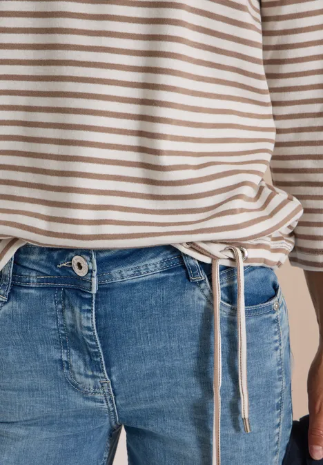 Beige-weiß gestreiftes Oberteil mit Tunnelzug am Saum kombiniert mit blauen Jeans.