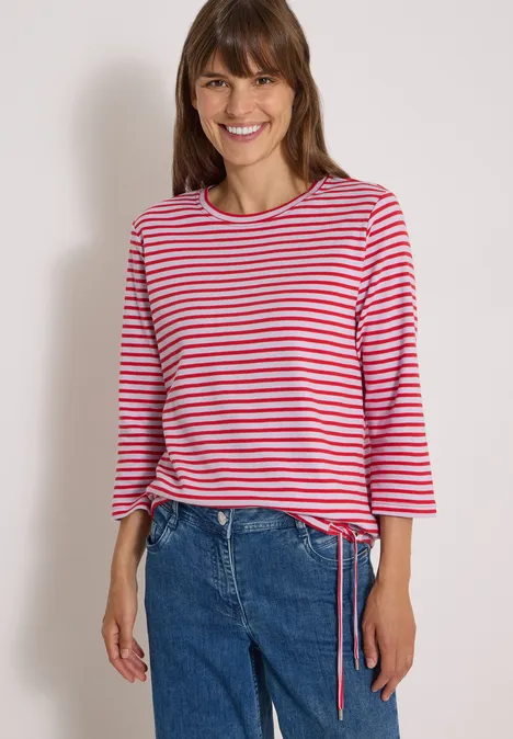 Frau lächelt in rot-weiß gestreiftem Shirt mit 3/4-Ärmeln und blauer Jeans.