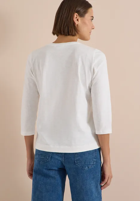 Femme de dos en t-shirt blanc à manches 3/4 et jean, fond beige.