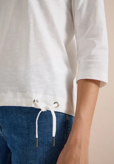 Gros plan sur un t-shirt blanc à manches 3/4 avec cordon et un jean bleu.