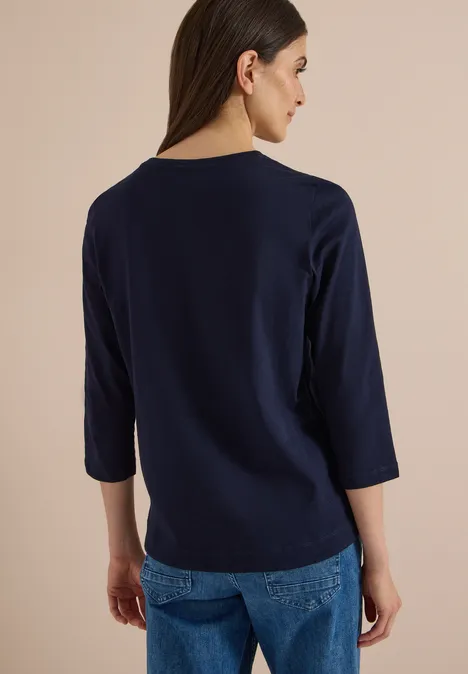 Vue de dos d'une femme portant un T-shirt bleu marine à manches 3/4 et un jean.