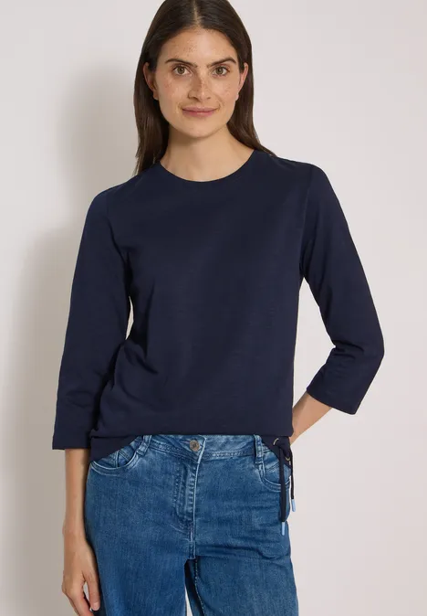 Femme portant un t-shirt bleu marine à manches trois-quarts avec laçage latéral et un jean.