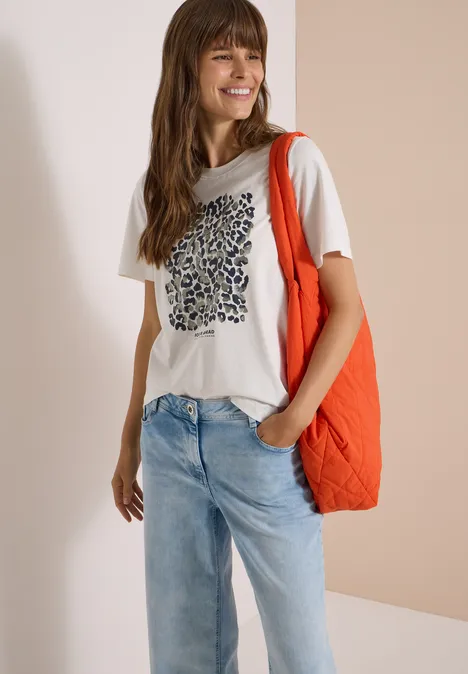 Shirt met luipaardprint en folie-details vanilla white Frau mit weißem T-Shirt, blauen Jeans, roter Tragetasche auf der Schulter, lächelnd vor hellem Hintergrund.