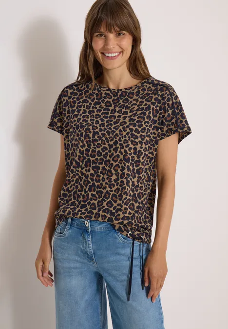 Lächelnde Frau im kurzärmeligen Leoparden-Shirt mit Kordelzug und Jeans.