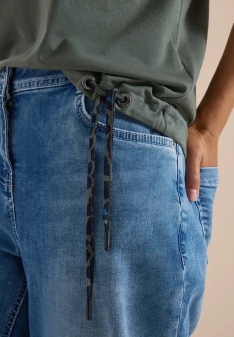 Nahaufnahme einer Person mit grünem Shirt und locker sitzender blauer Jeans mit Kordelzug-Bund.