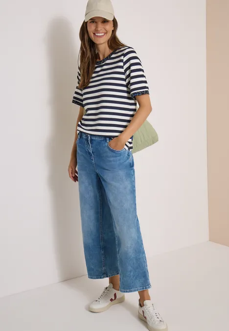 Frau trägt gestreiftes T-Shirt, weite Jeans, Cap und Stofftasche.