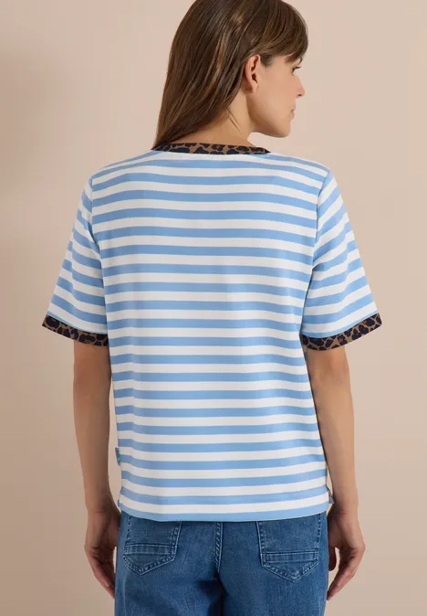 Person von hinten in weiß-blau gestreiftem T-Shirt mit Leo-Print am Kragen und Jeans.