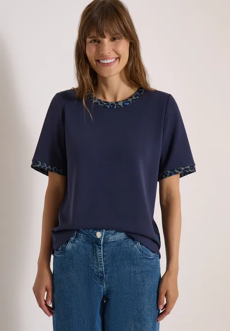 T-shirt à col rond avec des détails léopard urban dark blue Frau in dunkelblauem T-Shirt mit gemustertem Saum und blauer Jeans, lächelnd