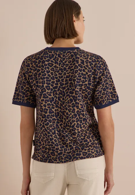 Rückenansicht einer Frau im kurzärmeligen Oberteil mit Leopardenmuster und heller Hose.