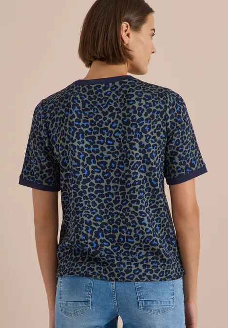 Frau steht von hinten, trägt blau-grünes Leo-Shirt und Jeanshose.