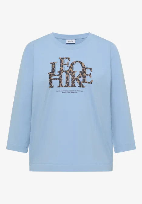Hellblaues Shirt mit 3/4-Ärmeln und braun-schwarzem Animal-Print-Schriftzug vorn.