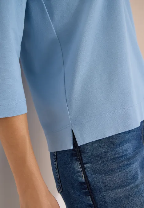 Person trägt hellblaues Shirt mit 3/4-Ärmeln und seitlichem Saumschlitz, kombiniert mit dunkler Jeans.