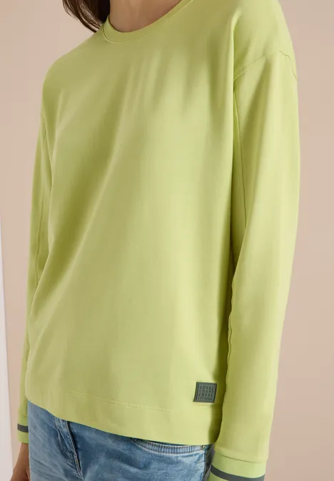 Eine Person trägt ein schlichtes, hellgrünes Langarmshirt aus weichem Stoff.