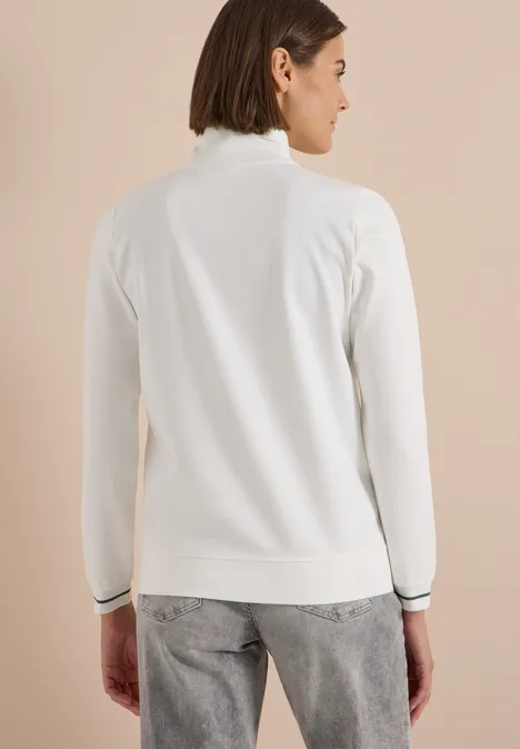 Rückansicht einer Person in weißem Rollkragenpullover mit schwarzem Saum.