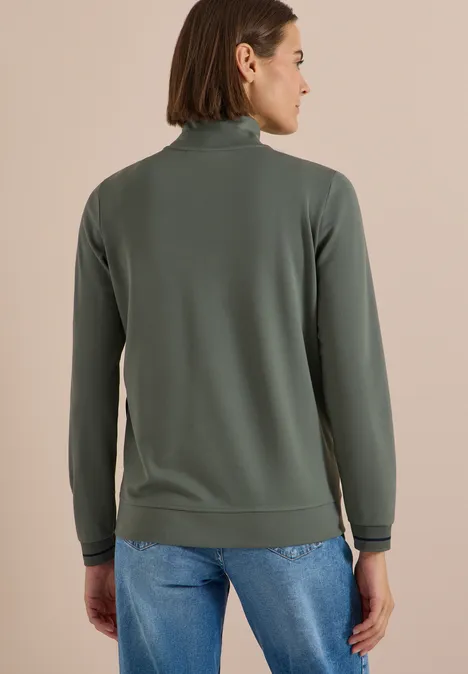 Frau von hinten in grau-grünem Rollkragenpullover und Jeans.