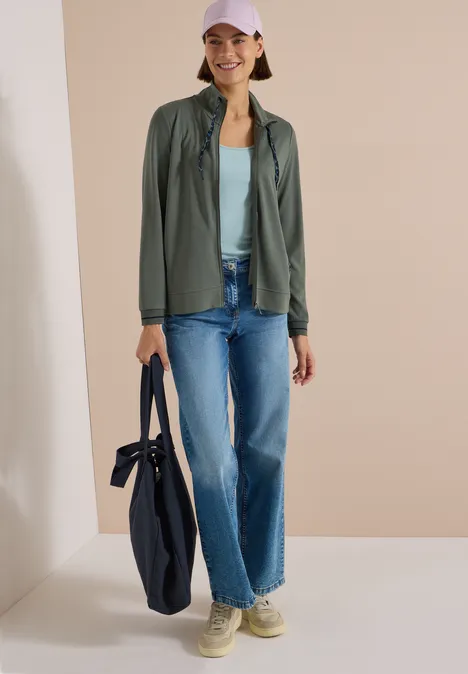 Junge Frau in lässiger Freizeitkleidung mit weitem Jeans, leichter Jacke, Cap und großer Tasche.