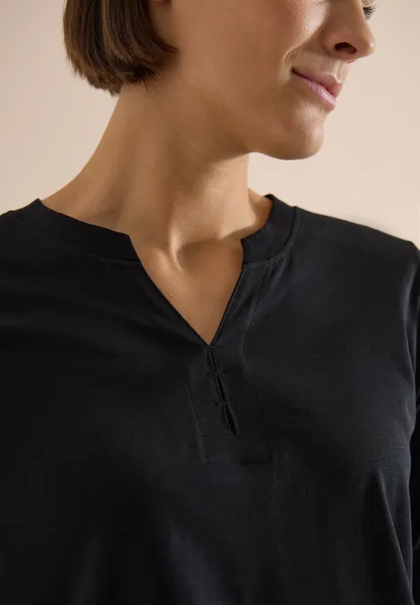 Nahaufnahme einer Frau im schwarzen Shirt mit V-Ausschnitt, Fokus auf Hals und Oberkörper.