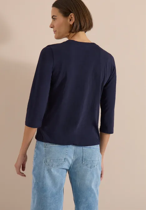 Person von hinten in marineblauem 3/4-Shirt und hellblauen Jeans.