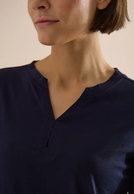 Frau trägt dunkelblaues Shirt mit V-Ausschnitt, Fokus auf Hals- und Schulterbereich.