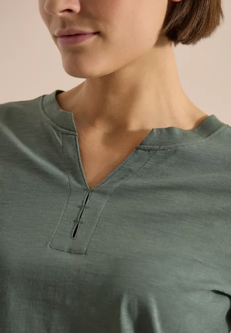 Nahaufnahme einer Frau im grünen T-Shirt mit V-förmigem Ausschnitt und Knopfdetail.