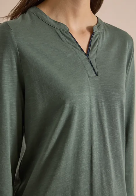 Nahe Ansicht eines grünen, langärmligen Damenshirts mit kleinem V-Ausschnitt und schwarzem Spitzenbesatz