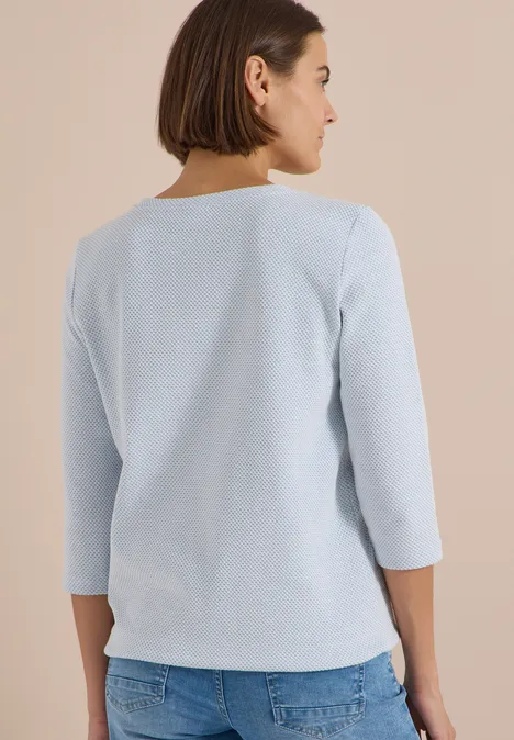 Frau von hinten in hellblauem 3/4-Ärmel-Oberteil und Jeans.