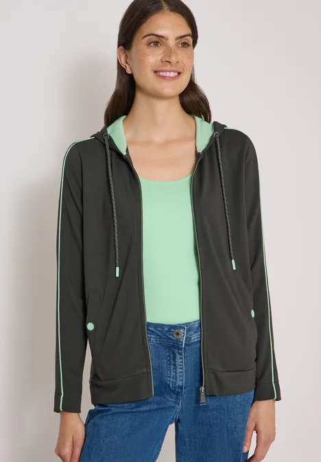 Jack met capuchon en contrasterende details raw khaki Vrouw glimlachend in een zwarte hoodie met mintgroen topje en jeans.