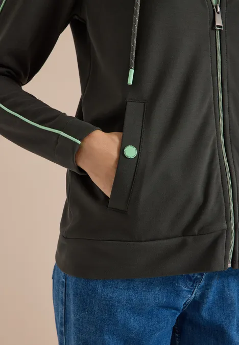 Jack met capuchon en contrasterende details raw khaki Zwarte hoodie met groene details aan ritssluiting en zak, blauwe jeans, hand in de zak