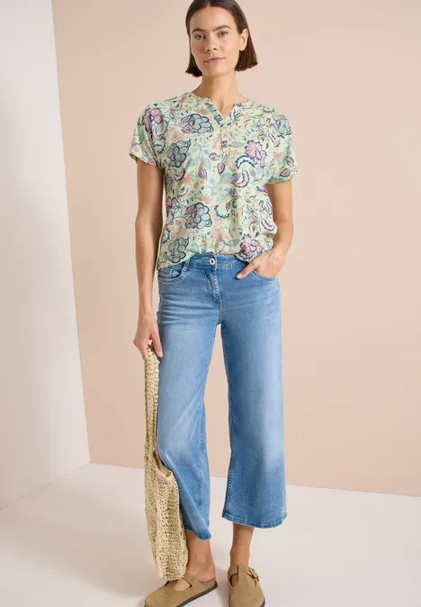 Frau trägt bunte Paisley-Bluse, helle Culotte-Jeans und goldene Tragetasche.