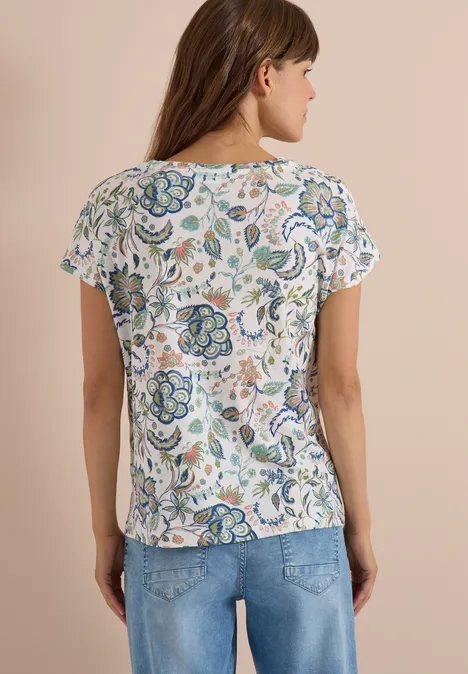 Vrouw van achteren in een witte korte mouw bloes met kleurrijk bloemenpatroon en blauwe spijkerbroek.