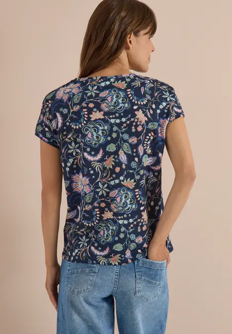Vrouw van achteren in een donkerblauw T-shirt met kleurrijk bloemenpatroon en spijkerbroek.