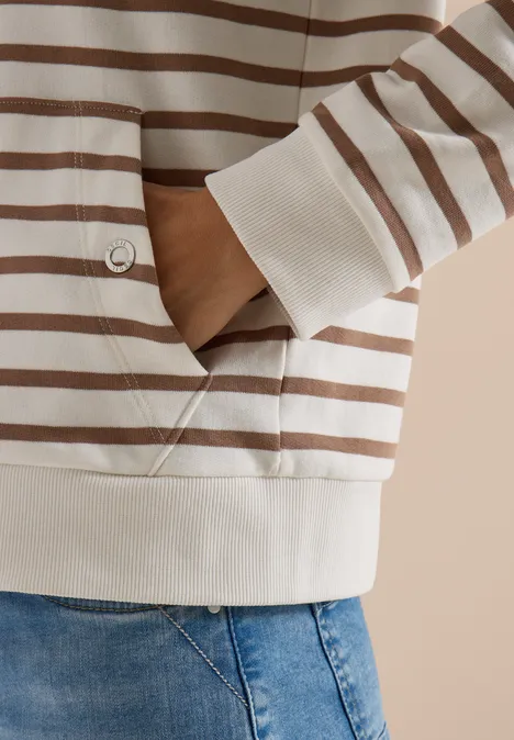Nahaufnahme eines Oberkörpers in beigebraun gestreiftem Pullover mit Hand in der Tasche und Jeans.