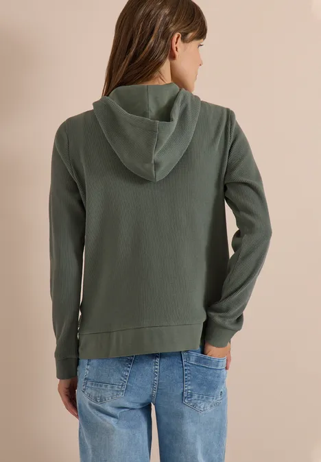 Person von hinten in grüner Kapuzenjacke mit Jeans.