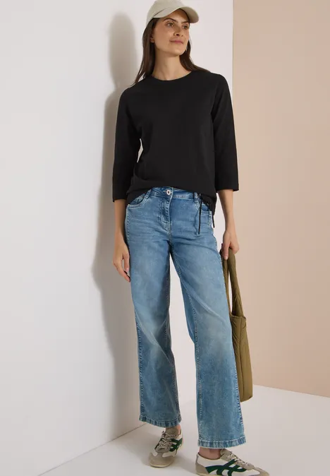 Frau trägt schwarzes Langarmshirt, helle Jeans, weiße Cap, olivgrünen Shopper und Sneaker.