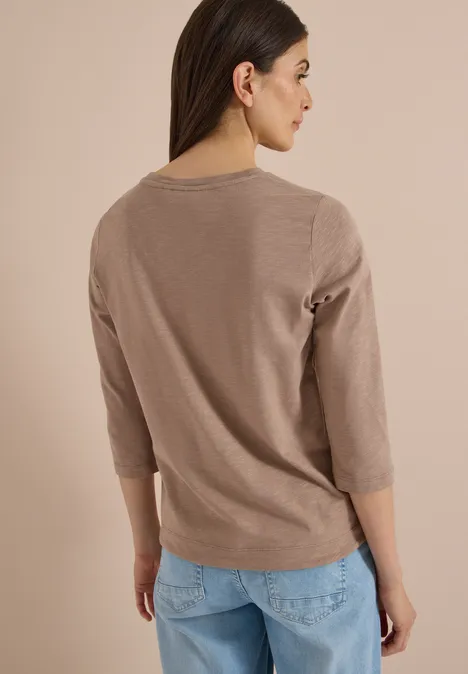 Frau von hinten, trägt beige 3/4-Arm-Pullover und helle Jeans.
