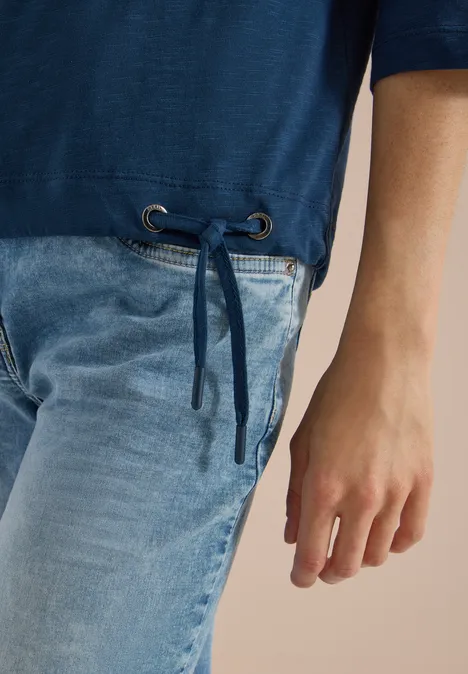 Blauer Pulli mit seitlichem Tunnelzug und hellblauen Jeans; Blick auf Taille und Hand.