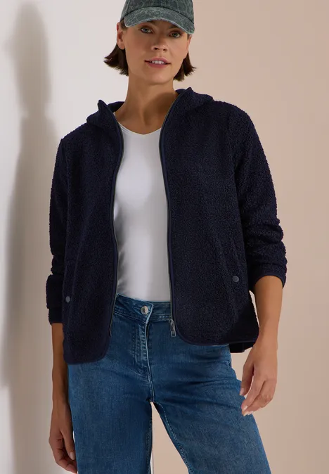 Teddy-Jacke mit Kapuze in Unifarbe urban dark blue Frau in dunkelblauer Fleecejacke mit Kapuze, weißem Shirt, Jeans und Baseballcap vor hellem Hintergrund.