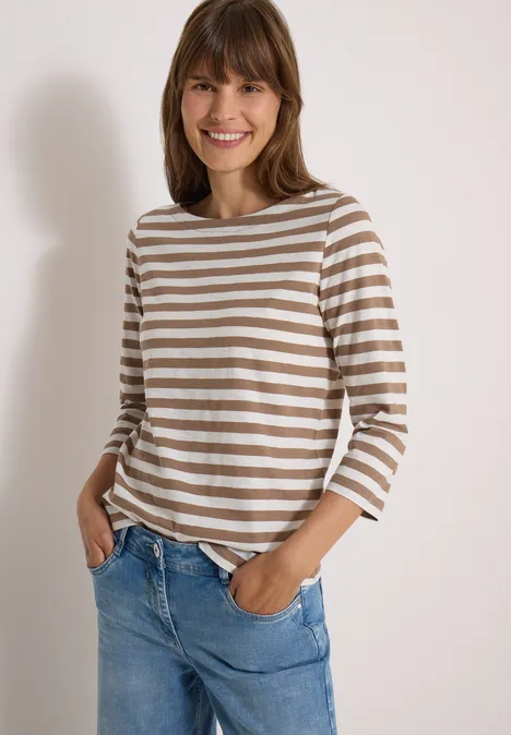 Basic Shirt met boothals en strepen natural taupe Fröhliche junge Frau mit braun-weißer Ringelshirt und blauen Jeans vor heller Wand.