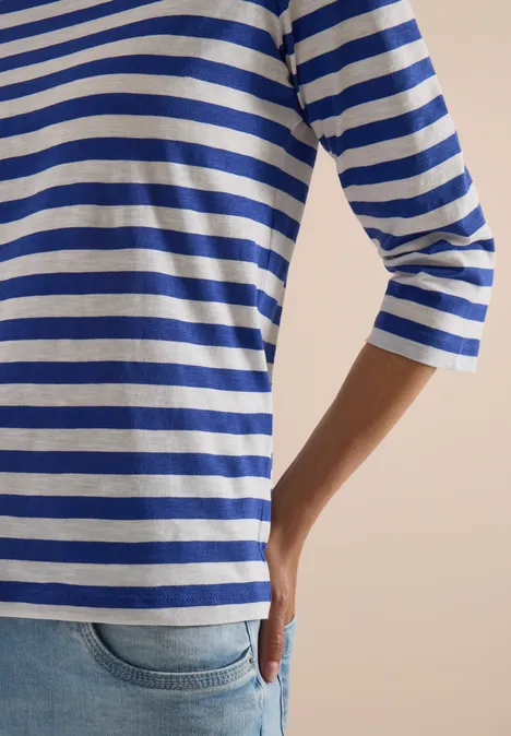 Oberkörper in blau-weiß geringeltem Dreiviertelarmshirt und Jeans, Hand locker am Rücken.