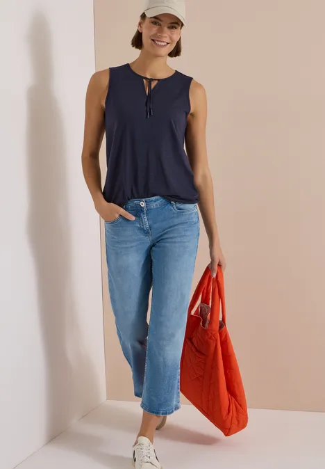 Frau in dunkelblauem Top, hellblauen Jeans, roter Tasche und Cap.