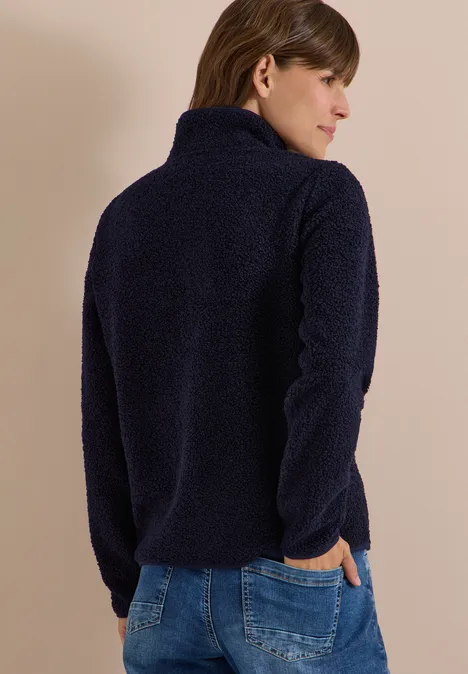 Frau von hinten in dunkelblauer Fleecejacke und Jeans vor neutralem Hintergrund.