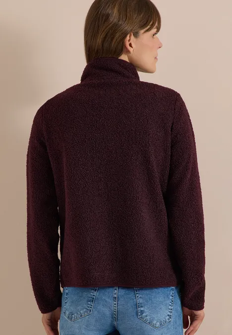 Rückansicht einer Frau in dunkelrotem, flauschigem Rollkragenpullover.