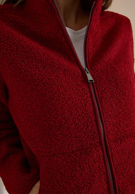 Nahaufnahme einer roten Teddy-Fleecejacke mit Reißverschluss und seitlichen Taschen, weißes T-Shirt darunter.