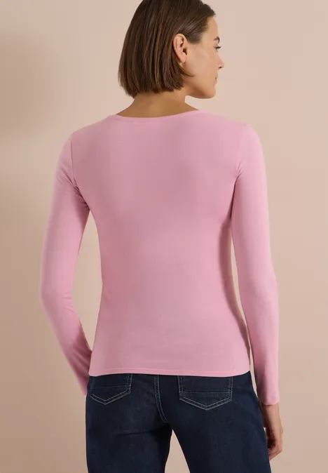 Frau in rosa Langarmshirt und Jeans, von hinten vor hellem Hintergrund.